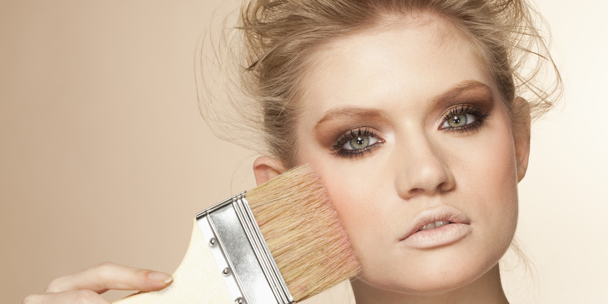 Portrait of young woman applying make up with paintbrush