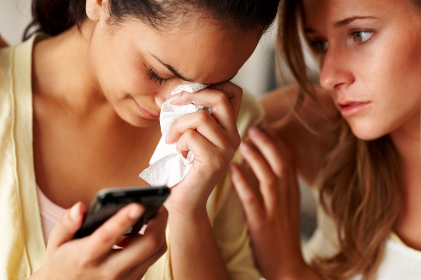 Closeup portrait of a young girl holding a mobile phone in sorrow with a friend consoling her