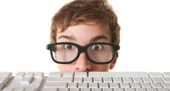 Surprised nerd hides behind a computer keyboard over white background